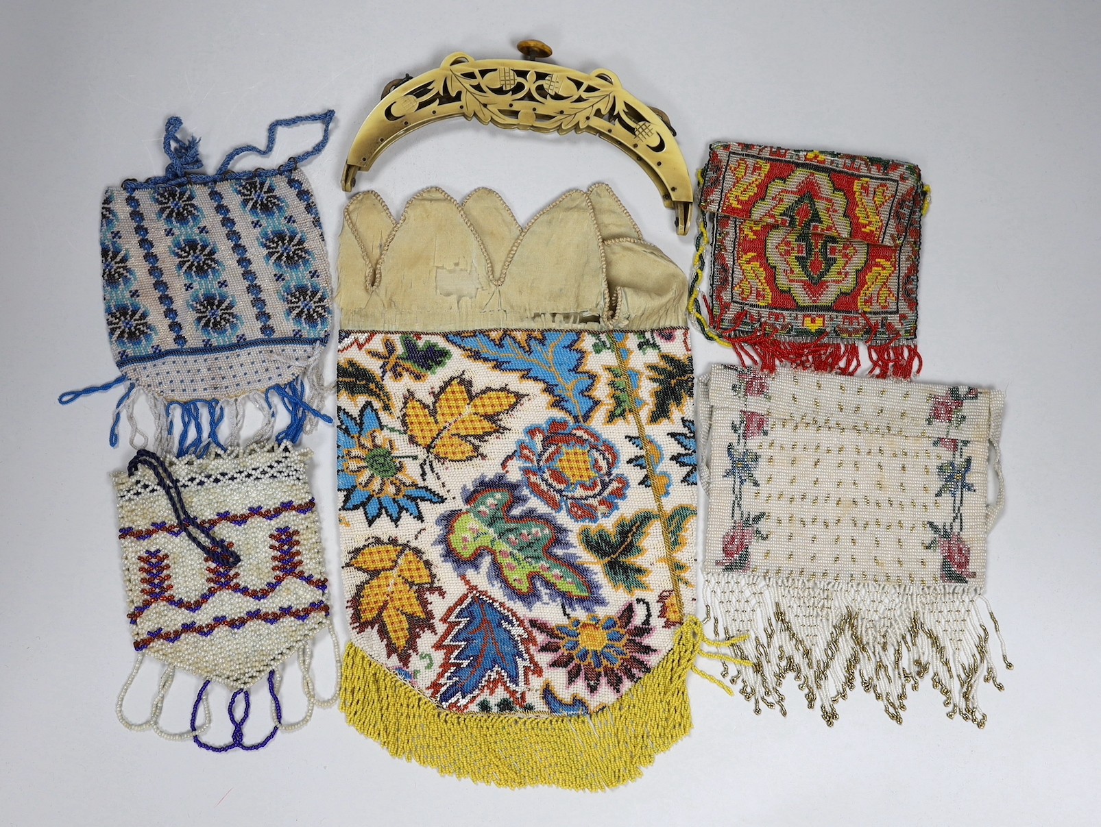 A 19th century ornately multicoloured beaded bag with a bead fringe, two smaller similar beaded purses a later coloured cut steel evening bag and a 1920’s Bakelite frame (6)